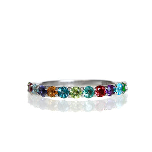 A product photo of a silver eternity band with 13 rainbow-coloured gemstones embedded along its length on a white background.