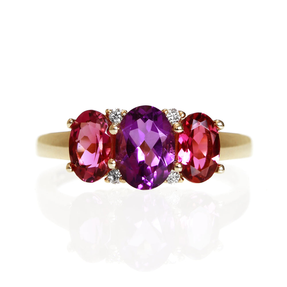 A product photo of a multi-gemstone Trio & Diamond Ring in Yellow Gold sitting on a plain white background. The largest amethyst centre stone measures 7x5mm, with 4 tiny diamonds nestled against it, two on each side. The smaller pink tourmaline stones are deep and warm, reflecting magenta hues across their multi-faceted edges.