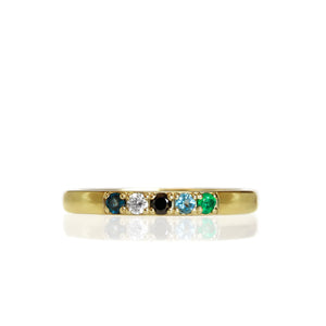 A product photo of a minimalistic 9 karat yellow gold stacking ring on a white background. The ring's band is smooth with a slight bevelled-edge, and has 5 2mm round mixed gemstones embedded along its length - Emerald, Aquamarine, Sapphire, White and Black Diamond.