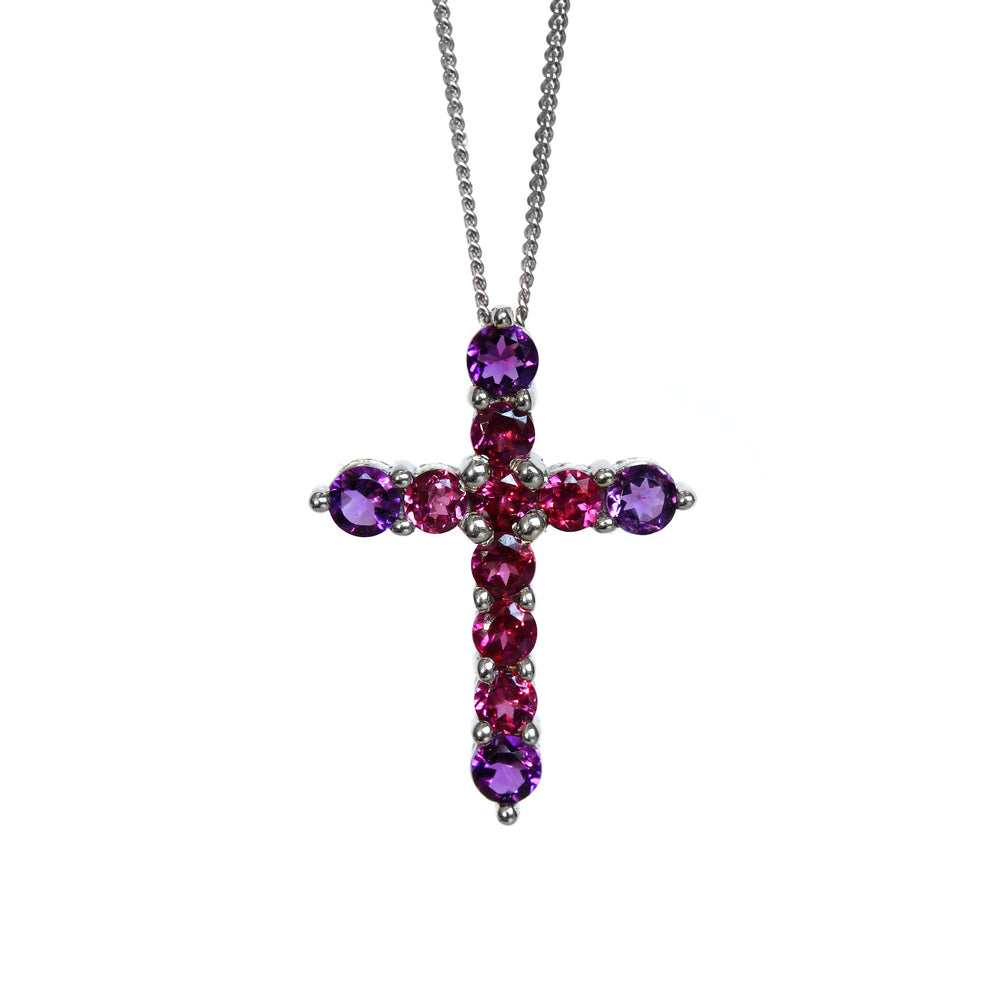 A product photo of a white gold cross pendant delicately bejewelled with multi-coloured gemstones suspended by a chain against a white background. The Christian cross pendant is made up of 11 stones in total, with the stones at the end of each prong being slighly bigger than the centre jewels.