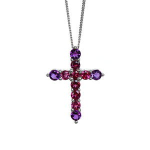 A product photo of a white gold cross pendant delicately bejewelled with multi-coloured gemstones suspended by a chain against a white background. The Christian cross pendant is made up of 11 stones in total, with the stones at the end of each prong being slighly bigger than the centre jewels.