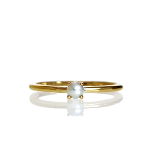 A product photo of a delicate yellow gold stacking ring with a tiny, claw-set white seed pearl in the centre sitting on a white background. The band is slim and thread-like, with the focus drawn to the petite 3mm opalescent pearl.