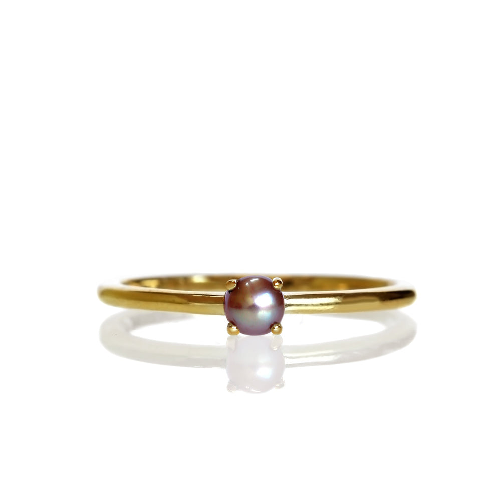 A product photo of a delicate yellow gold stacking ring with a tiny, claw-set greyish rosaline seed pearl in the centre sitting on a white background. The band is slim and thread-like, with the focus drawn to the petite 3mm opalescent pearl.