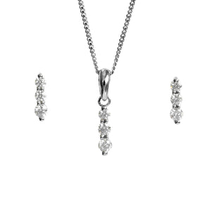 A product photo of a women's jewellery gift set in 9ct white gold and sparkling moissanite suspended against a white background. The white gold moissanite earrrings, each made up of 3 stones stacked vertically, descending from smallest to largest, sit on either side of a pendant of the same design suspended by a silver chain.