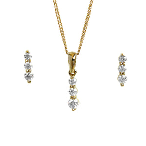 A product photo of a women's jewellery gift set in 9ct yellow gold and sparkling moissanite suspended against a white background. The yellow gold moissanite earrrings, each made up of 3 stones stacked vertically, descending from smallest to largest, sit on either side of a pendant of the same design suspended by a golden chain.