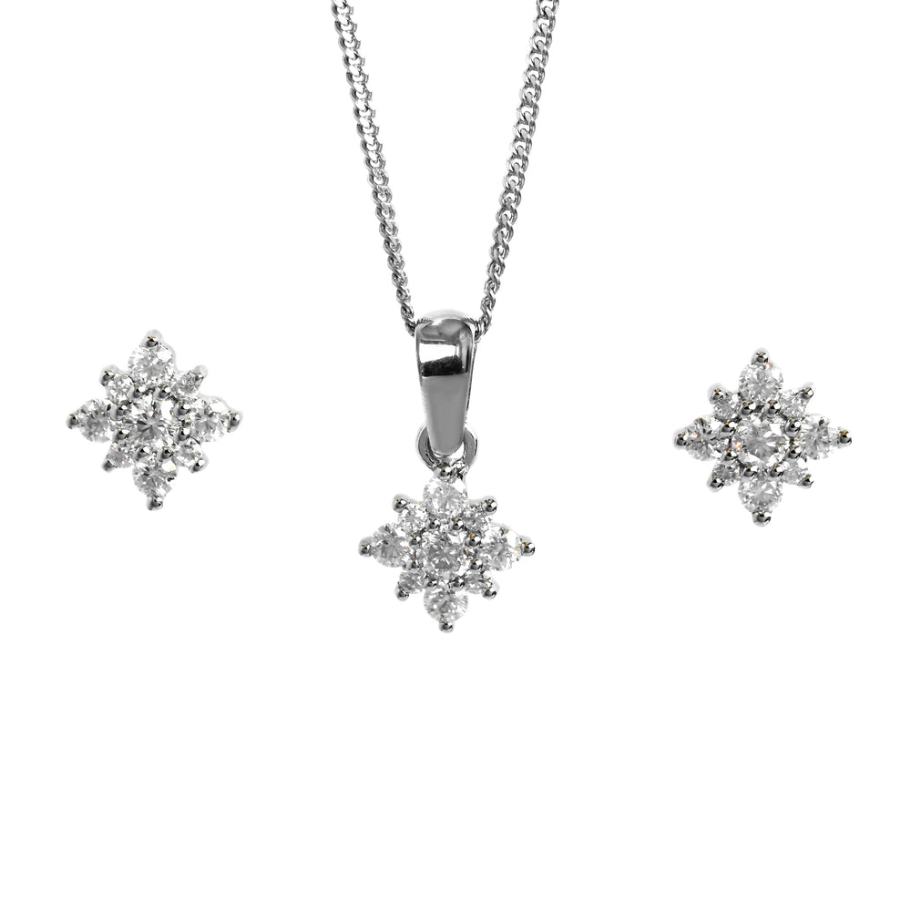 A product photo of a women's jewellery gift set in 9ct white gold and sparkling moissanite suspended against a white background. The white gold moissanite earrrings, each made up of glittering stones arranged in a floral or starlike formation, sit on either side of a pendant of the same design suspended by a silver chain.