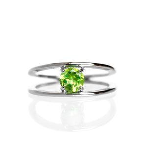 A product photo of a split-band sterling silver ring with a claw-set peridot centre stone sitting on a white background. The band splits at the base of the ring, separating to meet at the top and bottom of the chartreuse green cushion-cut centre stone, held in place by one tiny claw on each corner.