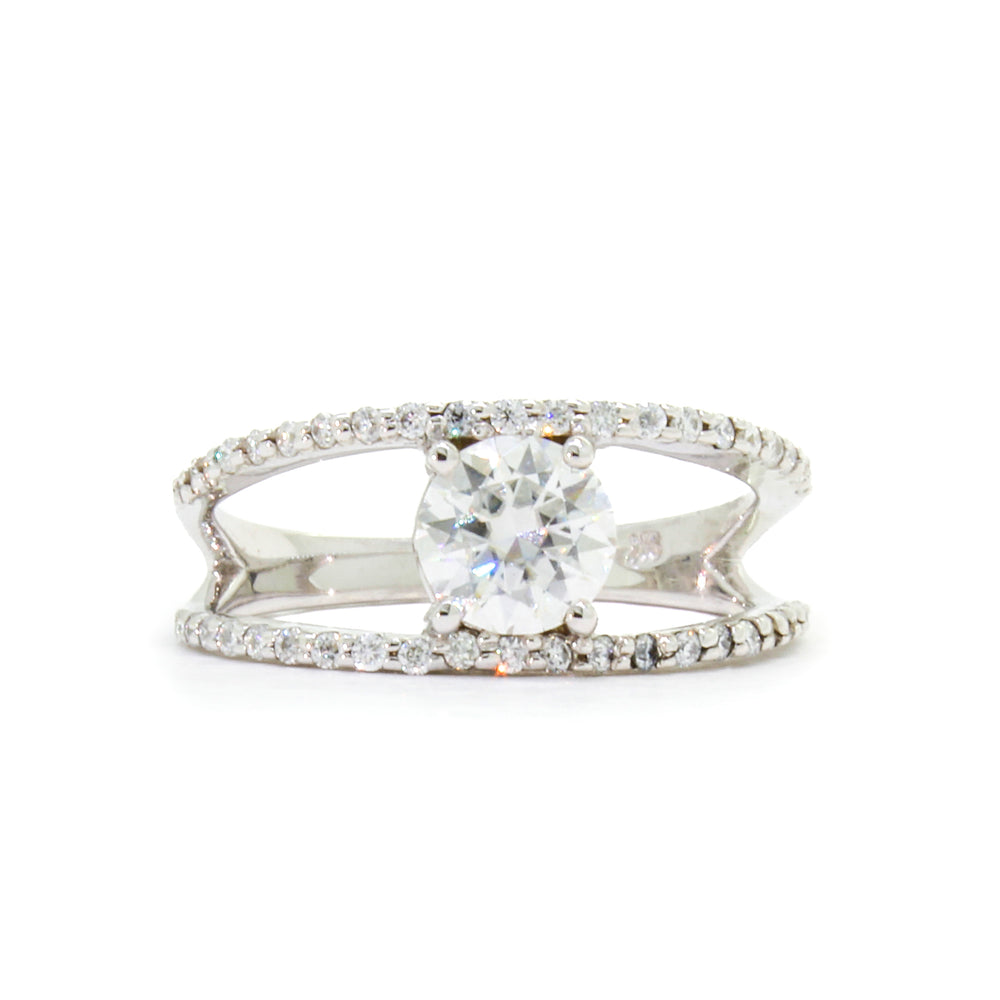 
            
                Load image into Gallery viewer, A product photo of a white gold moissanite ring sitting on a white background. The large moissanite gemstone is held in place by 4 claws. The white gold band splits halfway along its length into two smaller bands detailed with diamonds, and hug the centre stone&amp;#39;s top and bottom. 
            
        