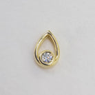 A product photo of a moissanite pendant in yellow gold sits on a clear white background. The pendant is in the shape of a small teardrop, with a petite gold-encased circle-cut moissanite gem nestled at its base. The yellow gold teardrop is smooth and unblemished. 